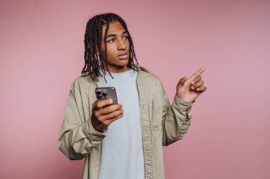 Saçları örgülü genç bir adam akıllı bir telefon tutuyor ve onu işaret ediyor..