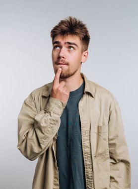 Rahat giyimli genç adam parmakları çenesinde düşünüyor..