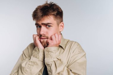 Endişeli bir ifadesi olan, tırnaklarını yiyen, bej gömlek giyen genç bir adam..