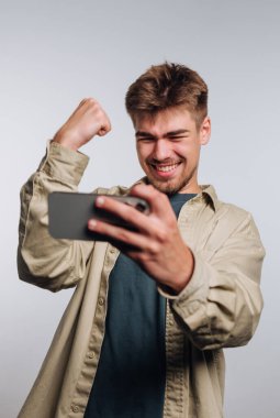 Genç adam akıllı telefona bakarken başarıyı kutluyor.