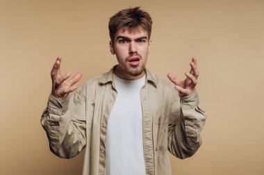 Bej arka planda elleri havada kafası karışmış genç bir adam..