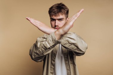 Genç bir adam kollarıyla bej arka planda X yapıyor..