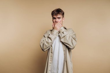 Ağzı ellerle kaplayan genç adam, şaşırmış ifade.