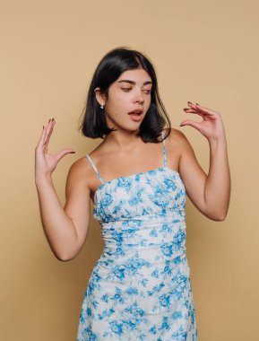 Çiçekli elbiseli genç kadın bej arka planda poz veriyor..