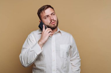 Beyaz gömlekli adam bej arka planda akıllı telefondan konuşuyor..