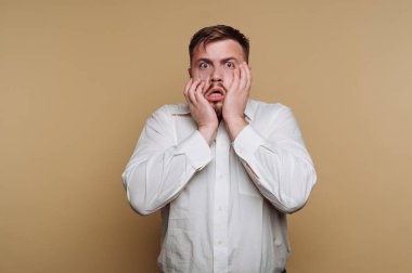 Beyaz gömlekli adam bej arka planda şok olduğunu söylüyor..