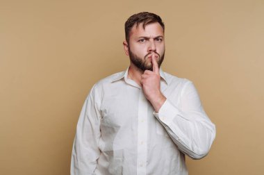 Beyaz gömlekli, bej arka planda düşünceli bir adam..