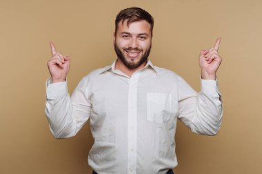 Beyaz gömlekli gülümseyen adam bej arka planda yukarıya bakıyor..