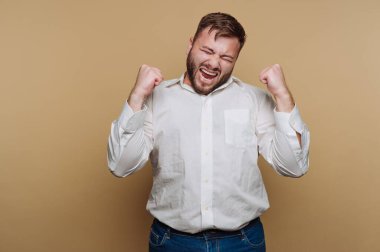 Beyaz gömlekli bir adam bej arka planda yumruklarını sıkarak kutlama yapıyor..