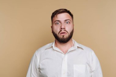 Beyaz gömlekli, bej arka planda sakallı, şaşırmış bir adam..