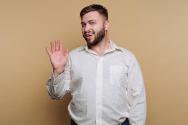 Gülümseyen adam bej bir arka plana el sallıyor..