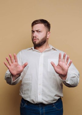Beyaz gömlekli, elleri havada bej arka planda dur işareti yapan adam..