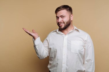 Beyaz tişörtlü gülümseyen adam açık elle el hareketi yapıyor.