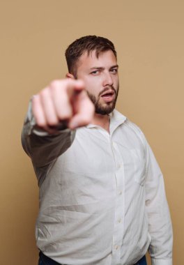 Beyaz gömlekli bir adam, bej arka planda, ciddi bir ifadeyle doğrudan kameraya bakıyor.