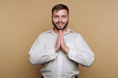 Elleri dua pozisyonunda, beyaz gömlekli, gülümseyen adam..