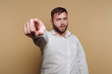 Beyaz gömlekli adam bej arka planda kameraya bakıyor.