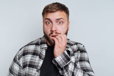 Şaşırmış bir yüz ifadesi olan, tırnaklarını yiyen, ekose gömlek giyen bir adam..