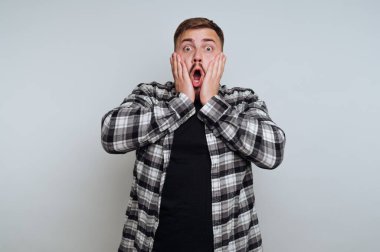 Ekose gömlekli, gri arka planda şaşırmış bir adam.