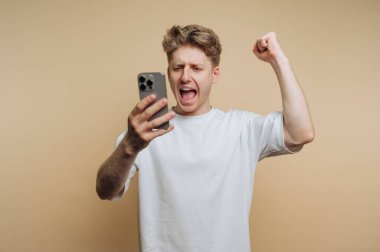 Akıllı telefona bakarken kutlama yapan heyecanlı genç adam.