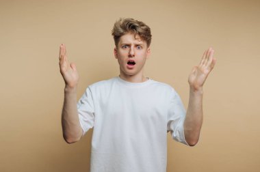 Bej arka plana el kaldırmış şaşırmış genç bir adam..