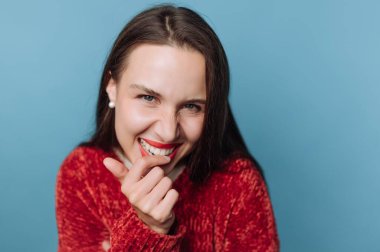 Bir kadının dişlerini gösterirken büyük bir gülümsemesi vardır. Parmağını ısırıyor ve kameraya bakıyor. Onun arka planı açık mavi bir renktir. Sahne kapalı bir yerde geçiyor..