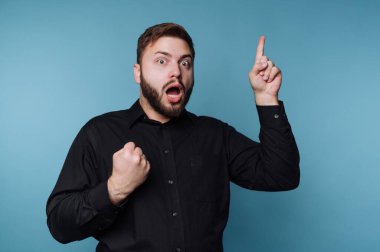 Mavi arka planı olan bir adam içeride duruyor. Açık bir ağzı ve şaşılacak şekilde geniş gözleri var. Bir el havaya kaldırılırken, diğeri yumruğunu sıkıca kavrıyor..