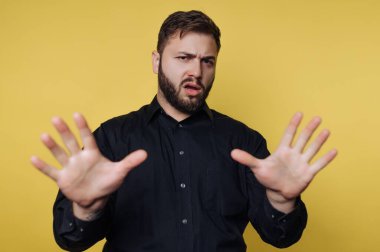 Parlak sarı bir arka planın önünde duran bir adam. Gelişigüzel bir ortamda şaşkınlık ya da şok yaşıyor gibi görünüyor..