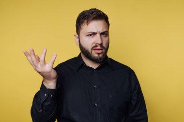 Yüzünde şaşkın bir ifadeyle bir adam ayakta duruyor. Karışıklık içinde bir elini kaldırdı. Arka plan parlak sarı. Dekor kapalı gibi görünüyor, muhtemelen sıradan bir yerde..