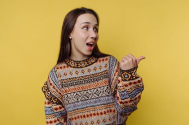 Sarı arka planı olan bir kadın stüdyoda duruyor. O, desenli bir kazak giyerken başparmağıyla gülümser ve el kol hareketi yapar. Sahne onun hareketli ifadesini ve rahat duruşunu yakalıyor..