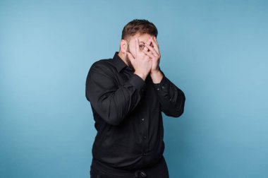 Stüdyoda mavi arka planı olan bir adam duruyor. Yüzünü elleriyle kapatıyor, bir anlık şaşkınlık ya da çekingenlik gösteriyor. Ayarlar basit ve sade..