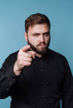 Bir adam mavi bir duvara karşı duruyor. Siyah bir gömlek giyiyor ve parmağını doğrudan izleyiciye doğrultuyor. Onun ifadesi ciddidir ve niyetini gösterir. Bu sahne kendine güvenmeyi gösteriyor..