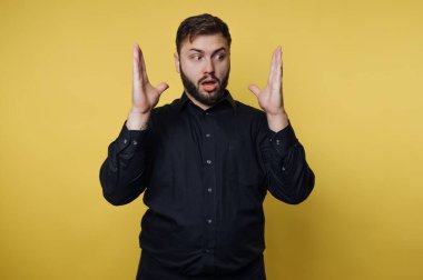 Bir adam içeride elleri açık, şaşkınlıkla dikiliyor. Yüzünde şok olmuş bir ifade var. Arka plan parlak sarı bir renktir. Ayarlar sıradan ve gayri resmi..