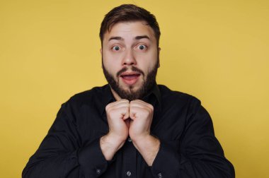 Sarı arka planı olan bir adam stüdyoda duruyor. O, geniş gözleri ve çenesinde elleri ile şaşkınlık gösterir. Heyecanlı ve meşgul görünüyor..