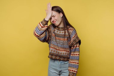 Sarı bir duvara karşı duran bir kadın. Onun uzun siyah saçları var ve renkli bir kazak giyiyor. Alnını tek eliyle tutarken hayal kırıklığına uğramış görünüyor..