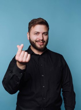 Siyah gömlekli bir adam mavi bir duvara dayanıyor. Gülümsüyor ve bir el hareketi yapıyor, dostane bir atmosfer yaratıyor. Bu sahne iyi ışıklandırılmış bir stüdyoda geçiyor..