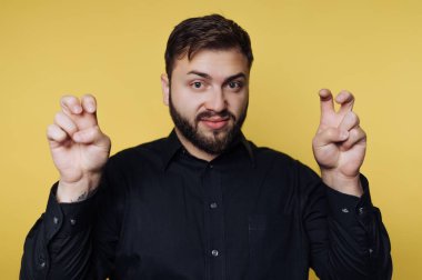 Bir adam parlak sarı bir duvarın önünde duruyor. O, kameraya bakarken parmaklarıyla eğlenceli bir jest yapıyor. Yüzünde neşe ve neşe ifadesi var..