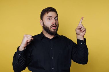 Sarı arka planda bir adam duruyor. Yüzünde şaşırmış bir ifade var, bir parmağını kaldırıyor ve yumruğunu sıkıyor. Onun ifadesi heyecan ya da farkındalık gösteriyor..