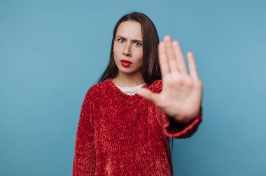 Bir kadın mavi bir arkaplanın önünde durur ve elini kaldırır. Yüzünde bir endişe ifadesi var. Bu sahne onun mesajına odaklanarak gün ışığında geçiyor..