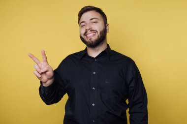 Bir adam sarı bir arkaplanın önünde duruyor. Gülümsüyor ve sağ eliyle bir barış işareti gösteriyor. Siyah bir gömlek giyiyor ve seans boyunca mutlu ve arkadaş canlısı görünüyor..