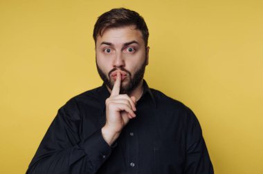 Sakallı bir adam sarı arka planda duruyor. Parmağı dudaklarında şşşş hareketi yapıyor. Ayarlar resmi görünmüyor.