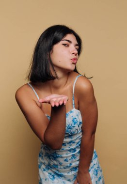 Genç bir kadın uzanmış bir elle durur ve bir öpücük savurur. Mavi çiçekli bir elbise giyiyor ve arkasında sade bir geçmişi olan uzun koyu renk saçları var..