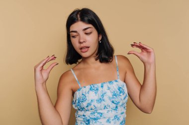 Stüdyo ortamında ellerini kaldırmış bir kız. Mavi çiçekli bir elbise giyer ve bir anlık ifadeyle yakalanır. Arka plan sarı..