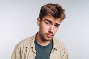 Genç bir adam rahat bir ifadeyle duruyor, basit bir tişört ve tişört giyiyor. Saçı şekilli ve hafifçe yana bakıyor. Arkaplan sade ve hafif.