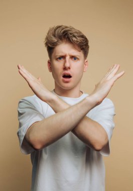 Tarafsız bir arkaplanın önünde duran genç bir adam. Kollarını önünde kavuşturmuş ve şaşırmış görünüyor. Kelimesiz iletişim kurarken ifadesi güvensizlik ya da şok gösteriyor..