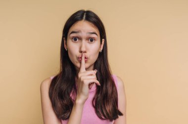 Genç bir kadın arka planda duruyor ve parmaklarını dudaklarına dayıyor. Doğrudan izleyiciye bakıyor. Onun jesti ile ifade edilen bir sessizlik anıdır..