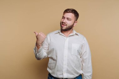 Bir adam basit, açık renkli bir arka plana karşı duruyor. Gülümsüyor ve parmağını kaldırıyor. Sıradan görünüşü dostane bir atmosfer olduğunu gösteriyor..