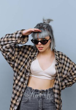 Ekose gömlek ve güneş gözlüğü takan bir adam açık mavi bir duvara karşı duruyor. Uzağa bakar gibi bir ellerini gözlerinin üstünde tutarlar. Bu sahne modern ve şık bir anı yakalar..