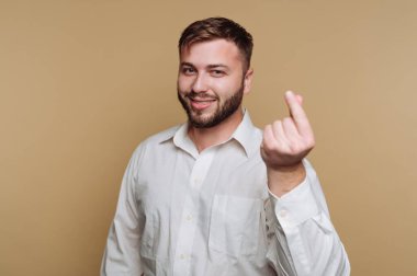 Sade bir geçmişi olan genç bir adam stüdyoda duruyor. O, parmaklarıyla bir jest yaparken gülümser. Resim neşeli ve neşeli bir anı yakalar..