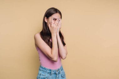 Bir kız ellerini yüzünü kapatarak içeride duruyor. O bir duygu ifade ediyor gibi görünüyor. Arkaplan koyu, açık sarı bir renktir. Gündüz oldu..