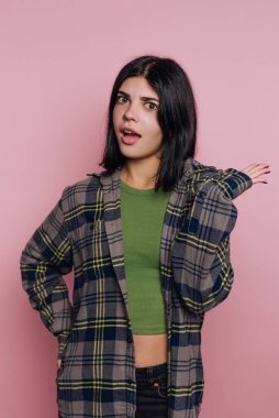 Genç bir insan şaşırmış bir şekilde duruyor, tek eliyle işaret ediyor. Yeşil bir gömlek ve kareli bir ceket giyiyorlar. Arkaplan pembe, ifadelerine zıtlık ekliyor..